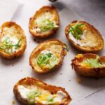 Air Fryer Potato Skins topped with melted cheese, sour cream, and sliced green onions are arranged on parchment paper for a deliciously crispy appetizer.