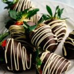 A plate of Chocolate Covered Strawberries dipped in dark chocolate and drizzled with white chocolate, arranged close together.