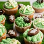Football Cupcakes with green frosting and football-themed decorations, including brown football-shaped cookies with white icing, are displayed on a grass-like surface.