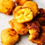 Close-up of several golden brown, breaded Mac and Cheese Balls, with one bite revealing the creamy pasta filling inside.