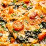 Close-up of Sheet Pan Pizza slices topped with melted cheese, cherry tomatoes, spinach, and fresh chopped herbs.