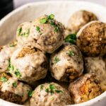 A bowl of vegetarian meatballs topped with creamy white sauce and garnished with chopped parsley.
