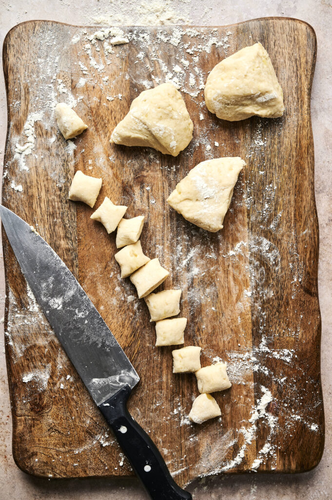 A floured wooden board with a chef’s knife and cut pieces of dough—some shaped into small segments, others in larger portions—ready to be transformed into Air Fryer Gnocchi.