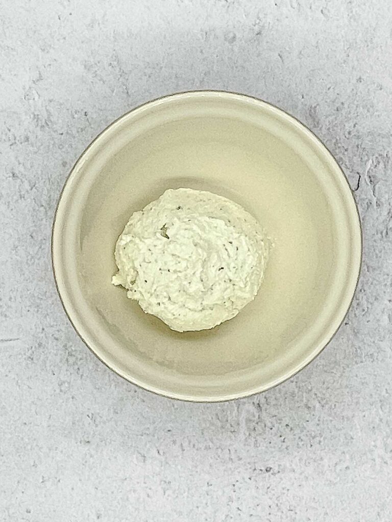 Overhead shot of a creamy goat cheese mixture with flecks of herbs in a ceramic bowl.