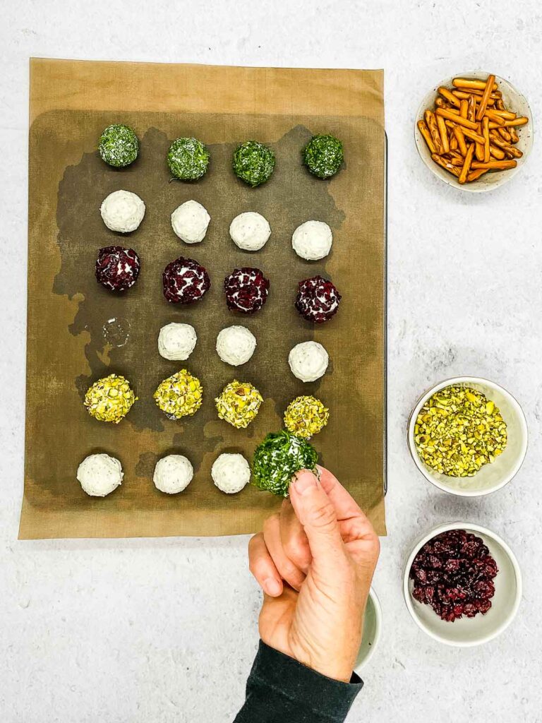 A hand holding a piece of food, delicately presenting one of the Mini Goat Cheese Balls.