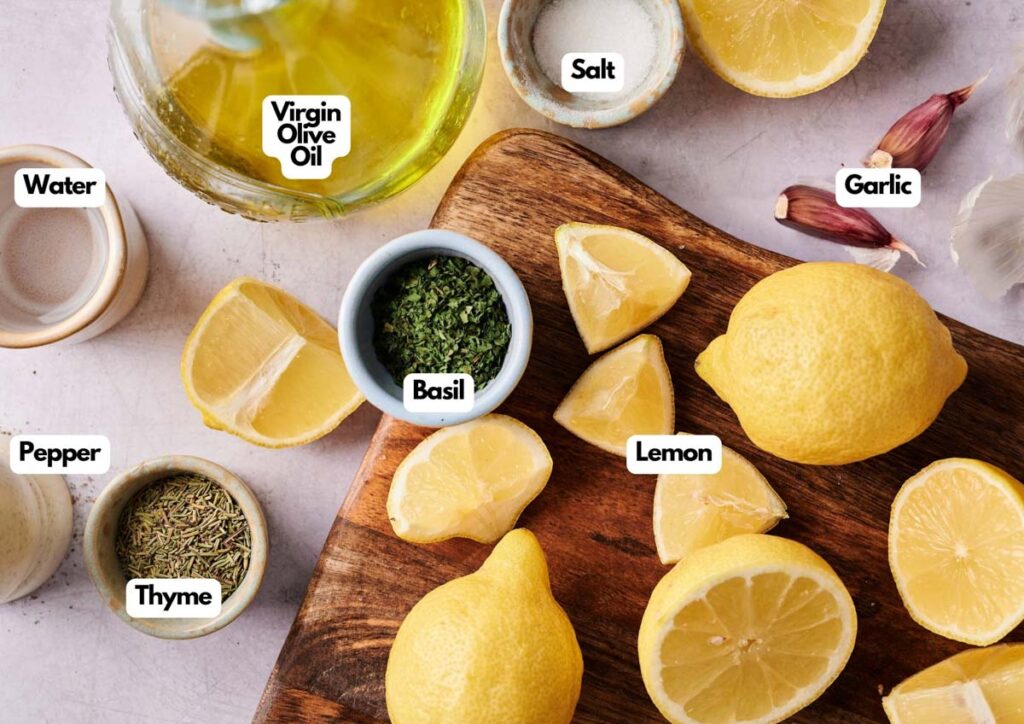 Overhead view of ingredients for Lemon Vinaigrette Dressing&mdash;virgin olive oil, salt, water, garlic, lemon, basil, thyme, and pepper&mdash;neatly labeled on a wooden board and countertop.