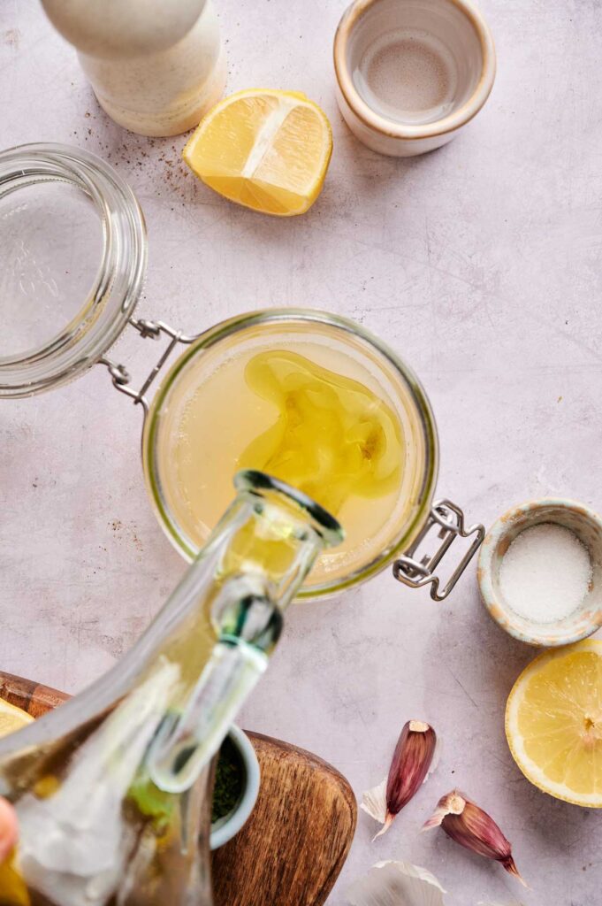 Olive oil is poured into a jar of lemon juice, ready to be shaken into a vinaigrette base.
