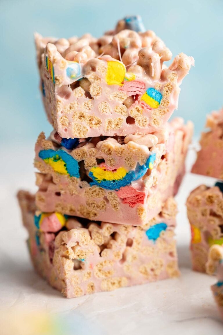 Three Lucky Charm Rice Krispy Treats stacked on top of each other, made with puffed cereal and colorful marshmallows, set against a light blue background.