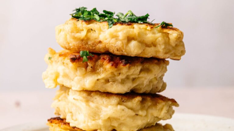 Three golden-brown potato pancakes are stacked on a plate, garnished with chopped herbs on top.