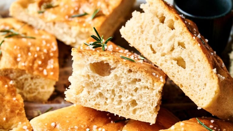 Close-up of sliced focaccia bread topped with coarse salt and rosemary, showing its airy, golden-brown interior.