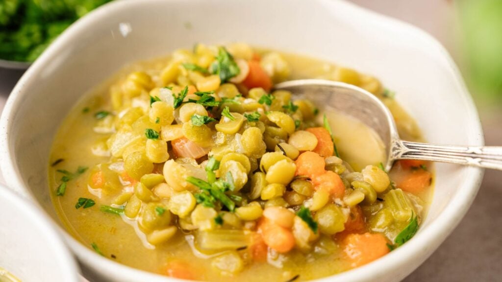 A bowl of split pea soup with chopped carrots, celery, and parsley, served with a spoon.