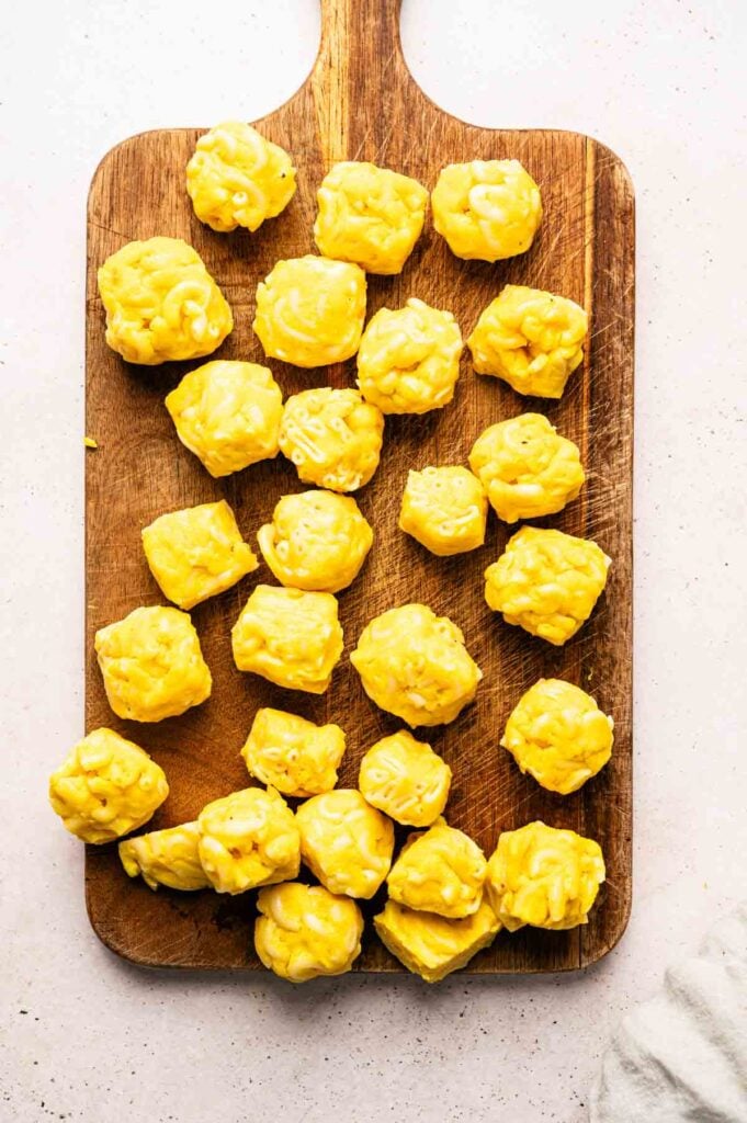 A wooden cutting board with several pieces of yellow siu mai dumplings and Mac and Cheese Balls arranged on top.