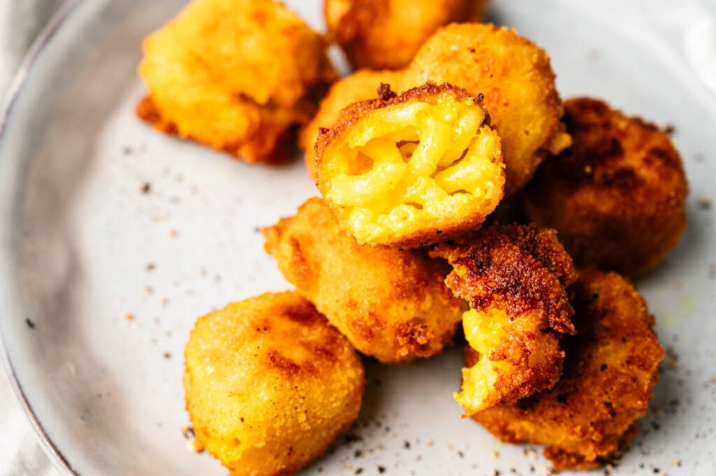A plate of breaded and fried Mac and Cheese Balls, with one piece broken open to reveal the gooey, cheesy filling inside.