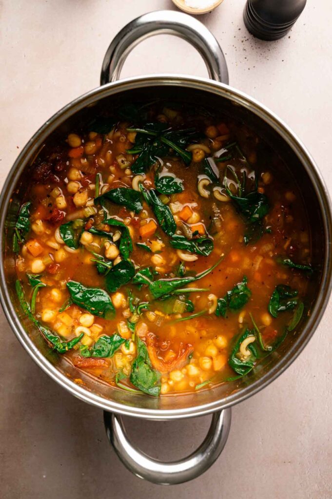 Fresh spinach wilts into the pot of chickpea soup, mixed with pasta and vegetables.