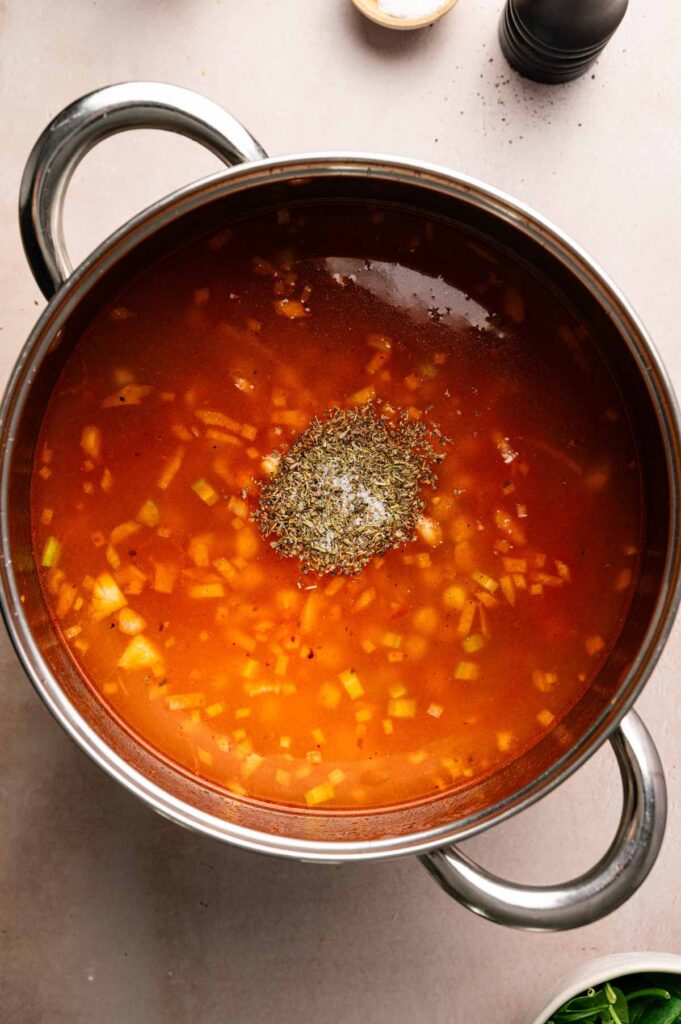 Vegetable broth is poured into the pot with Italian seasoning sprinkled on top, ready to be stirred in.