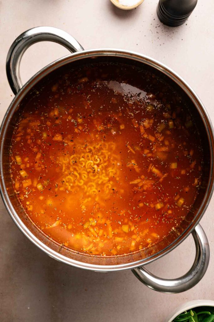 Small macaroni pasta is stirred into the simmering tomato broth, cooking until just tender.