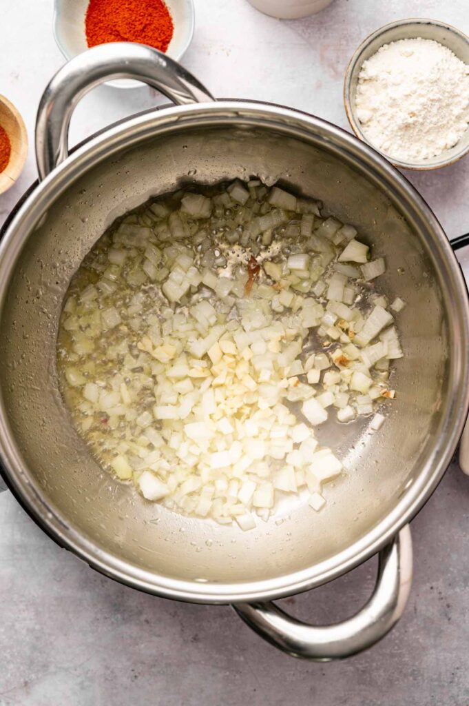 Diced onions and garlic sautéing in a pot, with smoked paprika and flour nearby.