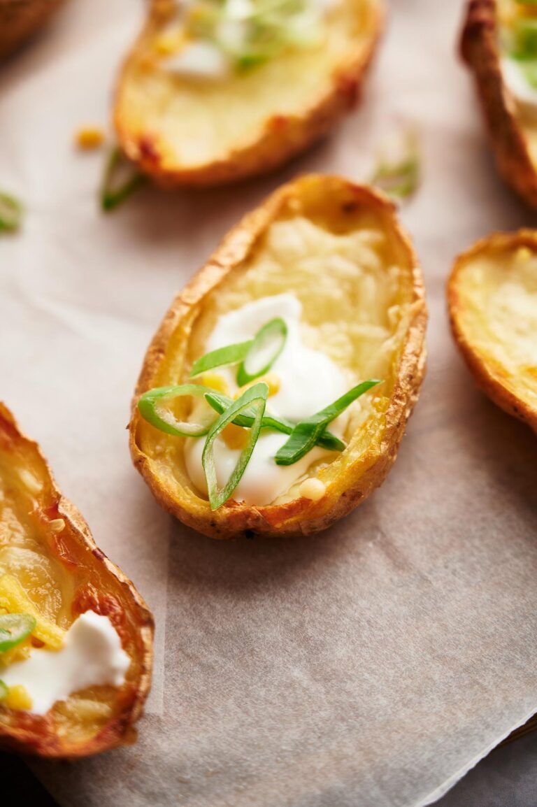 Loaded Potato Skins: A baked potato skin topped with melted cheese, sour cream, and sliced green onions, placed on parchment paper.