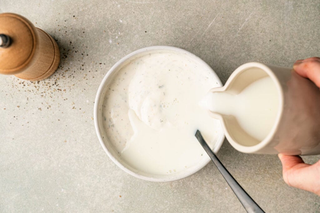 Milk is poured into a bowl of whisked ranch dressing base to thin it to the desired consistency.