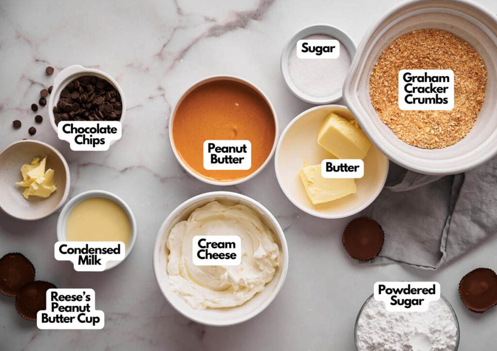 Assorted ingredients for a Reese's Peanut Butter Pie are arranged on a countertop, including cream cheese, peanut butter, butter, graham cracker crumbs, sugar, powdered sugar, condensed milk, chocolate chips, and peanut butter cups.