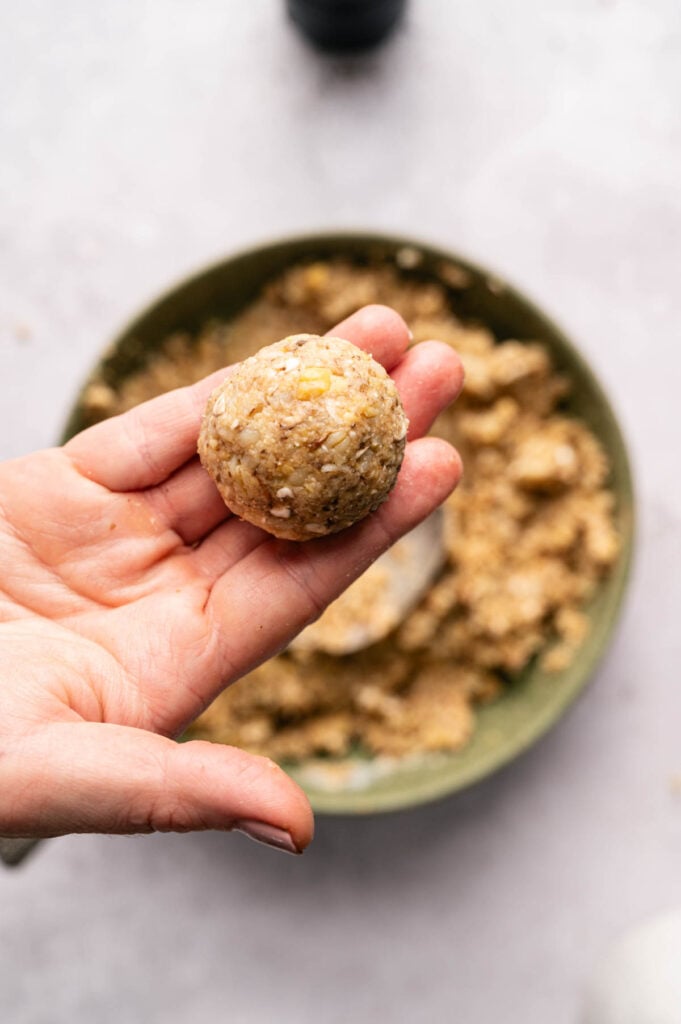 A hand holds a rolled vegetarian meatball above the bowl of mixture, showing the finished texture and size.