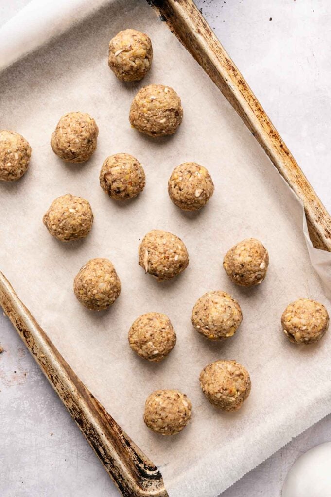 Rolled vegetarian meatballs are arranged on a parchment-lined baking sheet, ready to go into the oven.