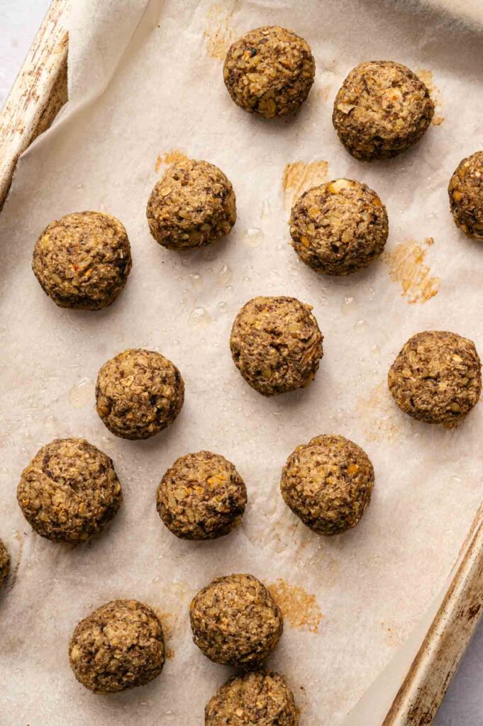 A baking sheet lined with parchment paper holds several evenly spaced, round, brown vegetarian meatballs, freshly baked.
