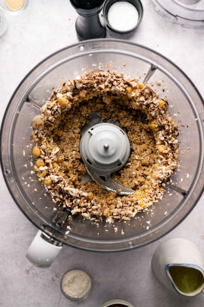 Finely chopped shiitake mushrooms and chickpeas sit in a food processor, ready to be transferred to a mixing bowl.
