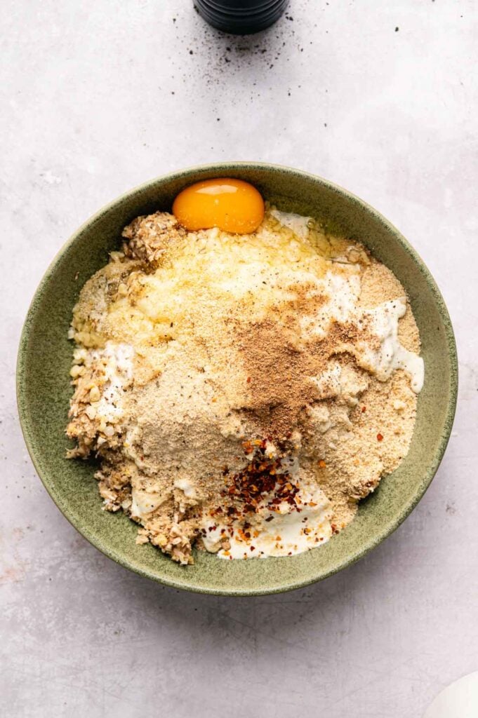 Bulgur wheat, breadcrumbs, an egg, and seasonings sit on top of the mushroom and chickpea mixture, ready to be combined.