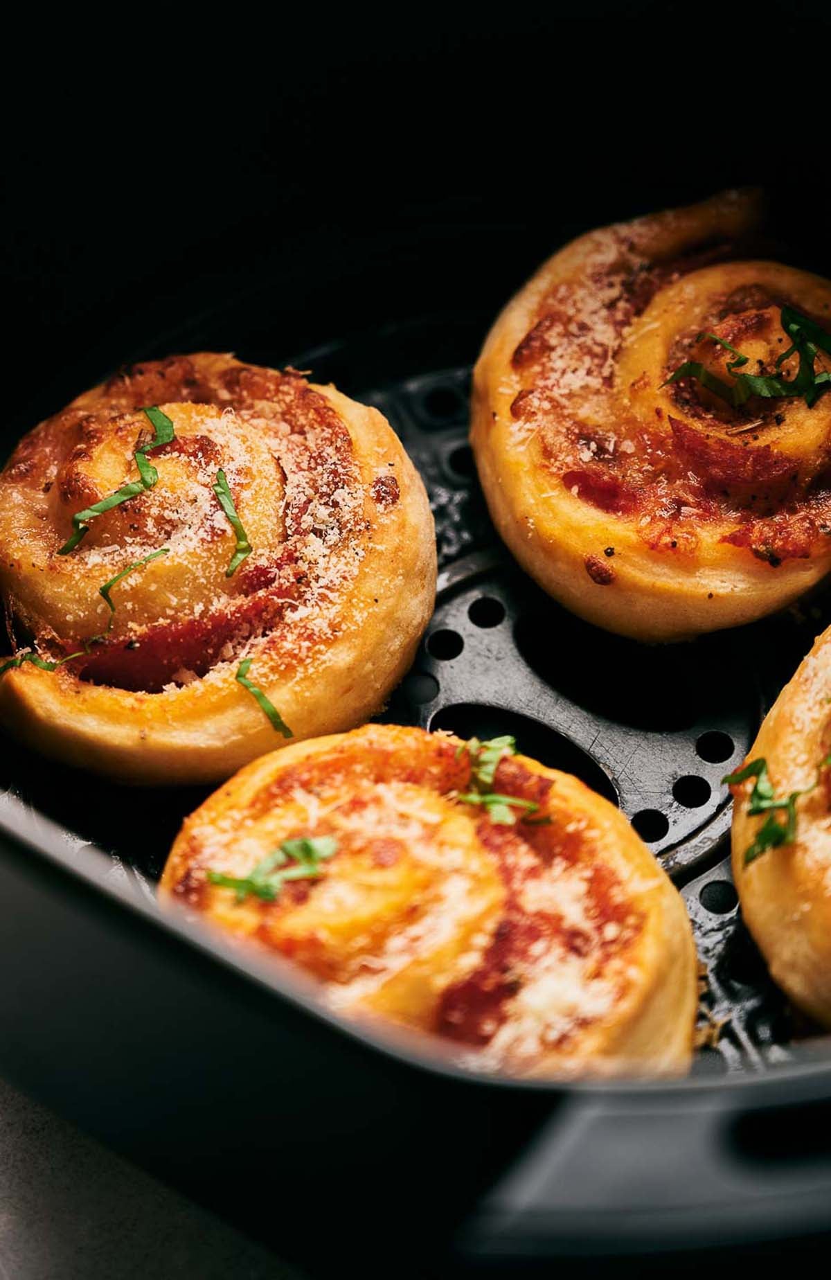 Four Air Fryer Pizza Rolls with visible cheese, tomato sauce, and herbs sit inside an air fryer basket.