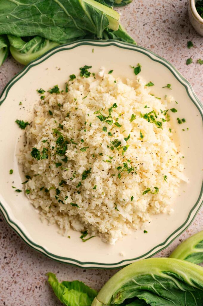 Cooked cauliflower rice is plated and garnished with fresh herbs and cracked pepper.