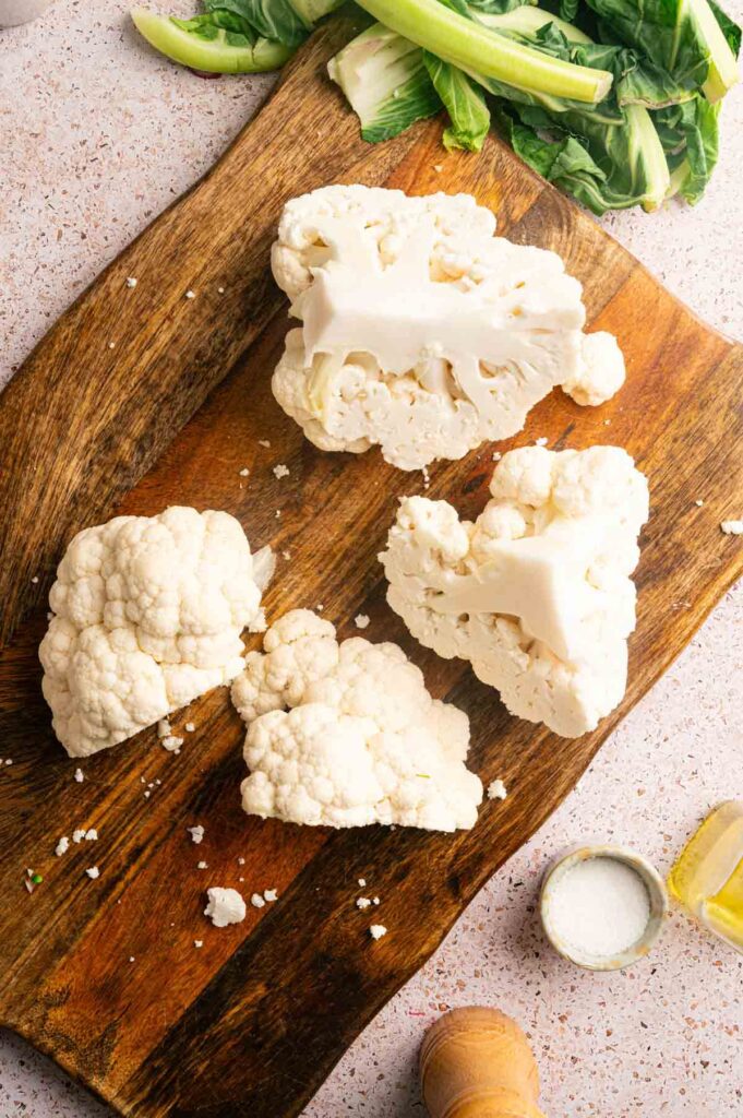 Quartered cauliflower florets sit on a cutting board with bok choy in the background.