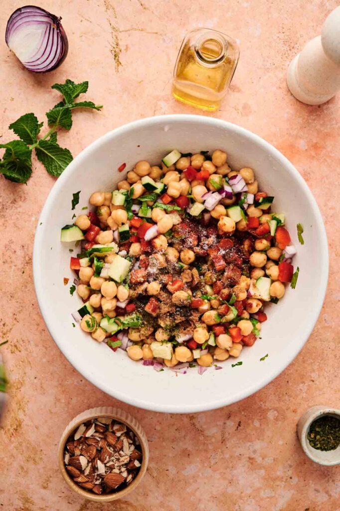 Ground spices are sprinkled over the mixed chickpea salad, ready to be tossed together.