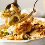 A close-up of a spoonful of cheesy Broccoli Casserole being lifted from the dish, revealing gooey melted cheese and a perfectly browned topping.