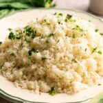 A plate of cooked Cauliflower Rice garnished with chopped herbs and black pepper.