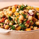 A vibrant Chickpea Salad featuring chopped red onions, tomatoes, fresh herbs, crunchy almonds, and diced yellow bell peppers in every bowl.