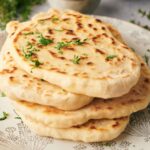 Three pieces of flatbread naan stacked on a patterned plate, garnished with chopped fresh herbs.