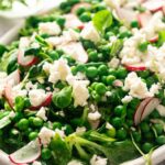 A fresh Pea Salad with green peas, spinach, sliced radishes, and crumbled white cheese served in a white dish.