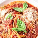 Plate of Spaghetti Marinara with tomato sauce, topped with grated cheese and fresh basil leaves.