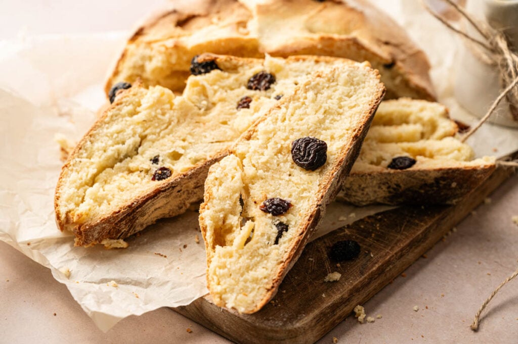 Sliced loaf of Irish Soda Bread with raisins rests on parchment paper atop a wooden board.
