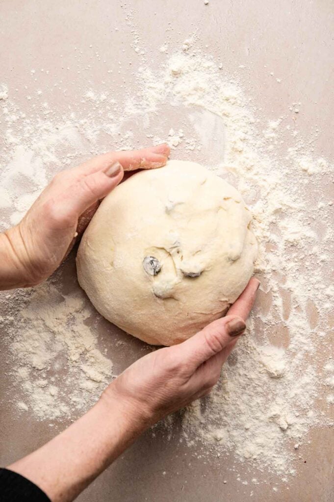 Hands shaping a round ball of Irish Soda Bread dough on a floured surface.