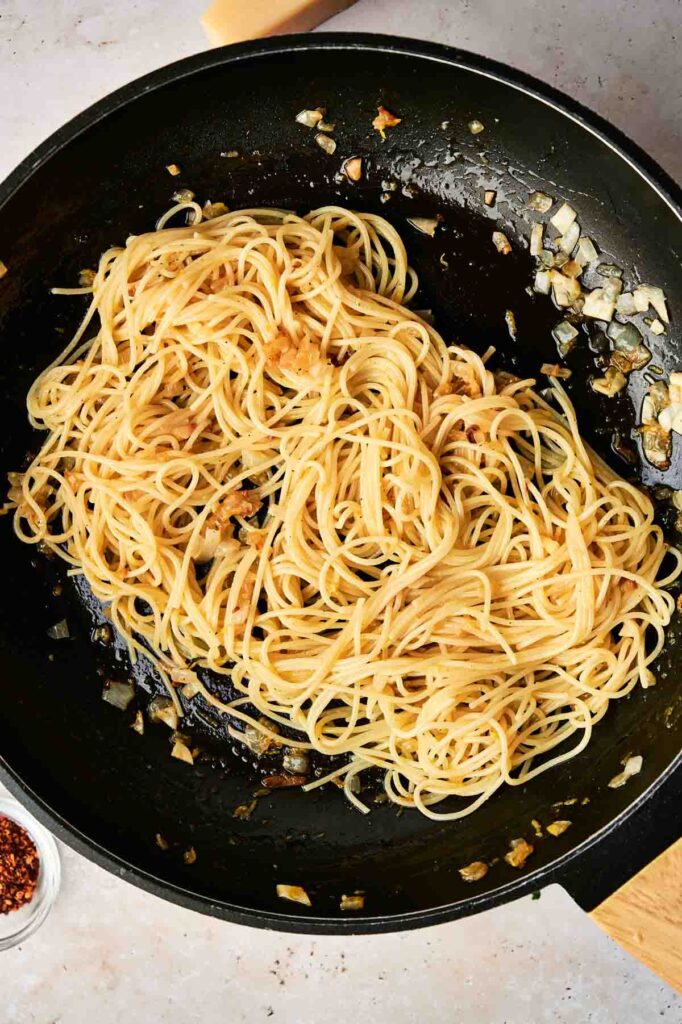 Cooked Lemon Pasta with saut&eacute;ed onions and garlic in a black frying pan, viewed from above.