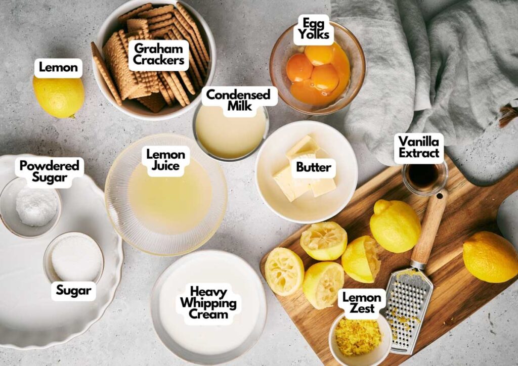 Top-down view of labeled ingredients for Lemon Pie, including graham crackers, lemon, powdered sugar, sugar, lemon juice, heavy whipping cream, condensed milk, egg yolks, butter, vanilla extract, and lemon zest.