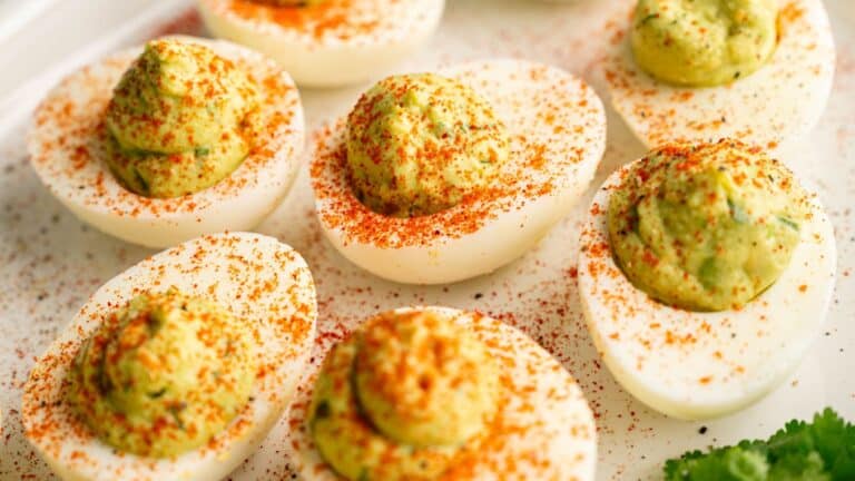 A plate of deviled eggs topped with a greenish filling and sprinkled with red paprika.