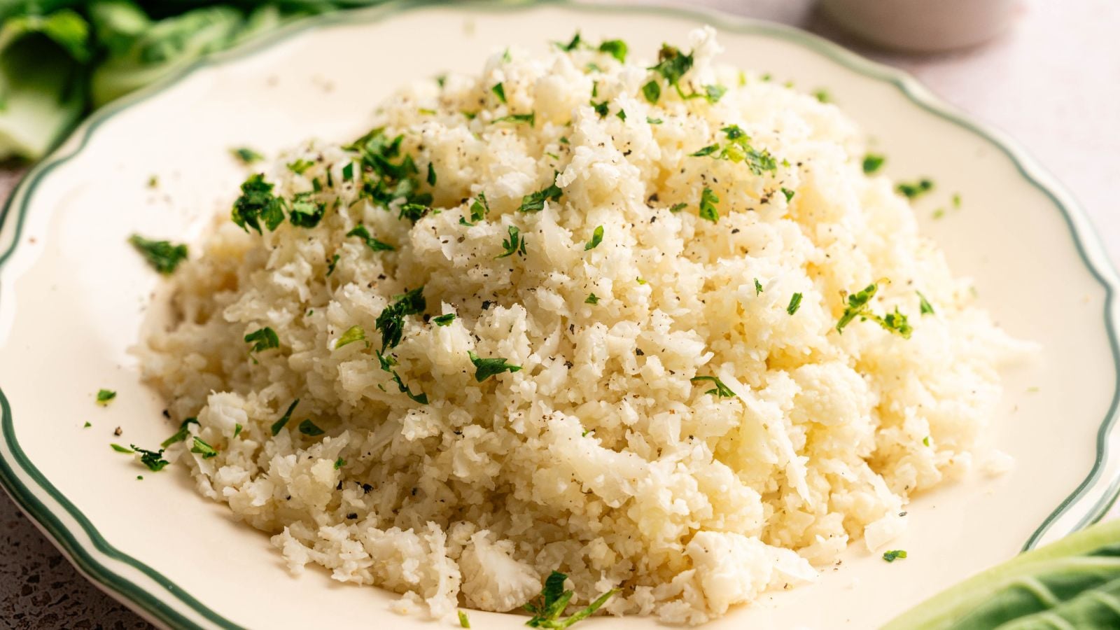 A plate of cauliflower rice garnished with chopped parsley and black pepper.