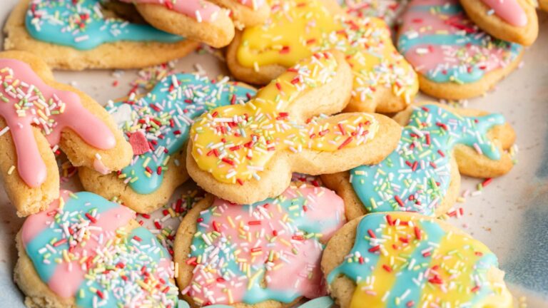A pile of sugar cookies shaped like bunnies and eggs, decorated with colorful pastel icing and rainbow sprinkles.