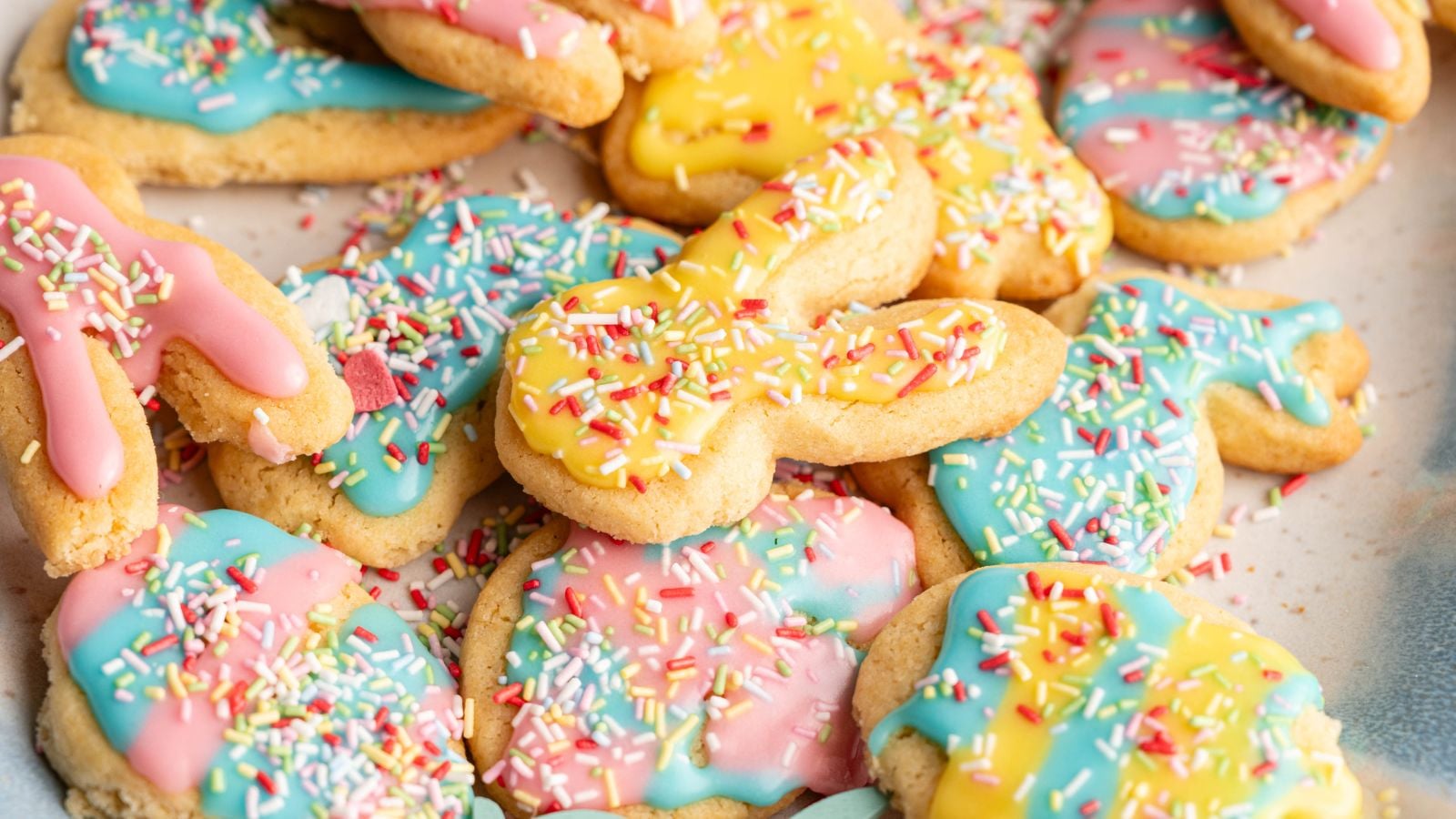 A pile of sugar cookies shaped like bunnies and other forms, decorated with pastel pink, yellow, and blue icing and topped with colorful sprinkles.