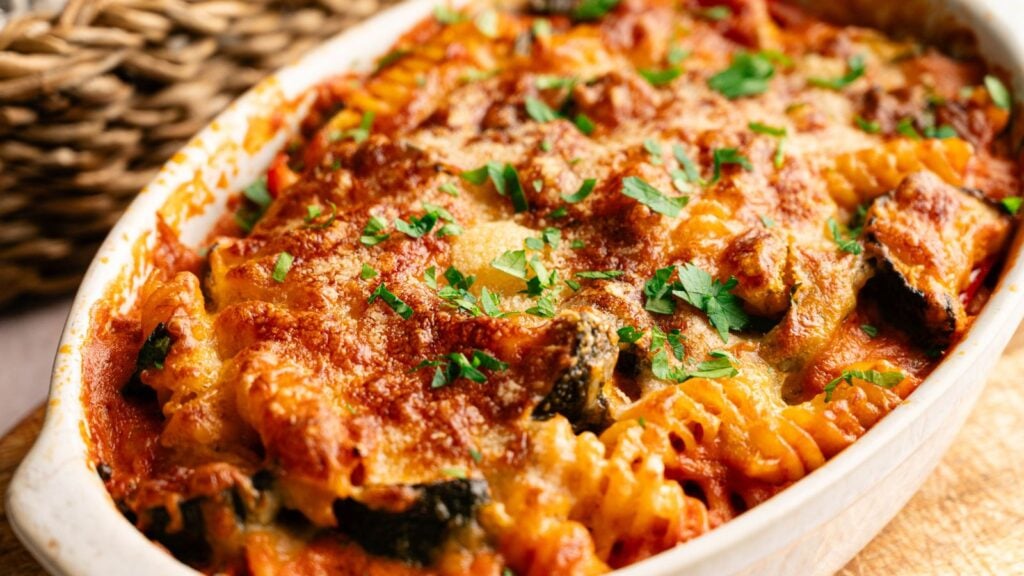 A baked pasta casserole with rotini, tomato sauce, melted cheese, and parsley garnish in a white oval dish.
