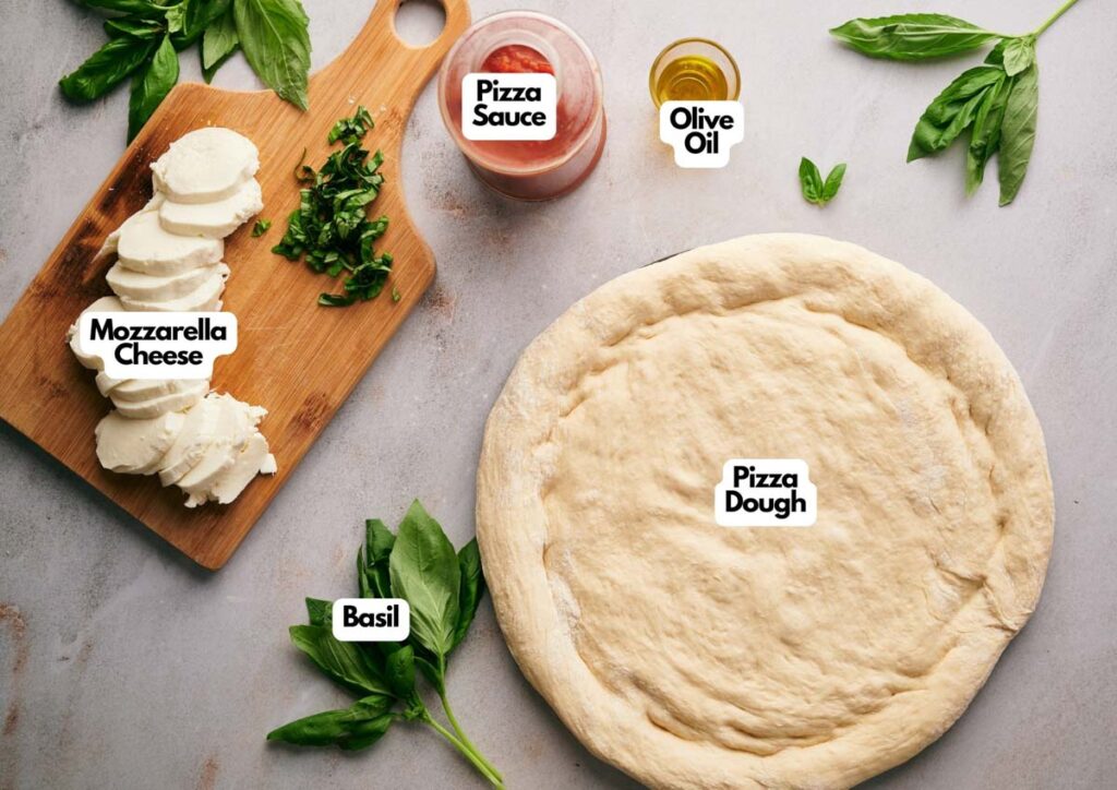 A Neapolitan Pizza dough crust rests on a countertop, surrounded by fresh basil, olive oil, pizza sauce, sliced mozzarella cheese, and chopped basil on a wooden board.