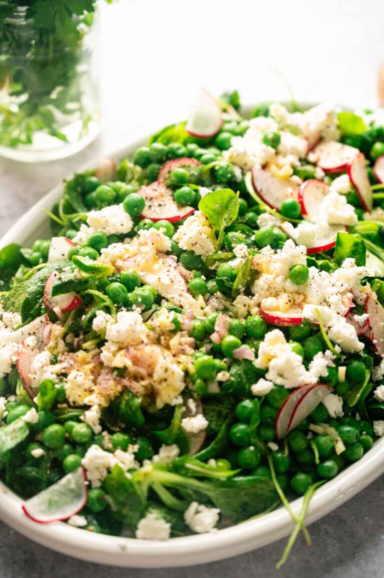 A refreshing Pea Salad platter featuring green salad with peas, radish slices, crumbled feta cheese, leafy greens, and a light dressing.